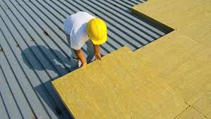 Construction worker fitting stone wool insulation panels on an industrial roof to maximize building energy performance